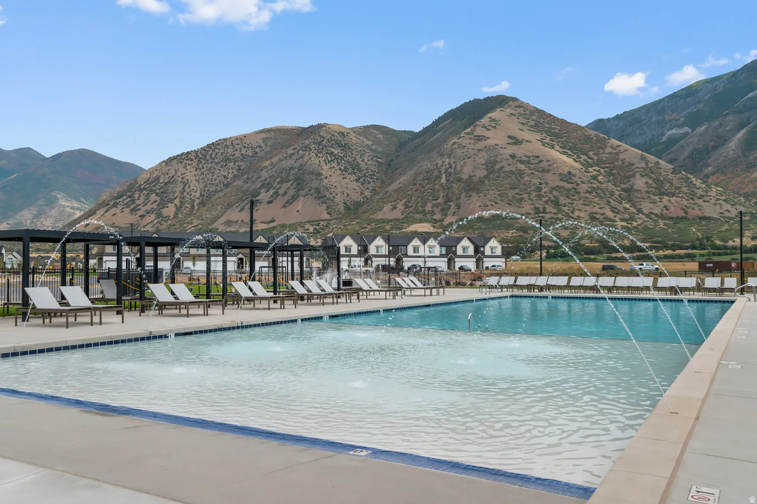 Resort-style pool with integrated water features, expansive sundeck, multiple lounge chairs, and pergolas