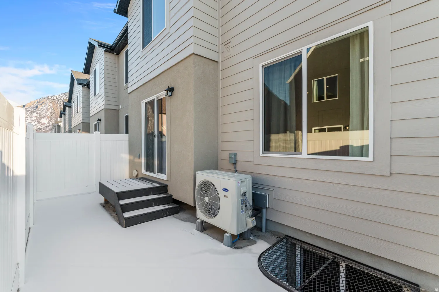 Enclosed outdoor area featuring a privacy fence, sliding glass door entry, exterior lighting fixture, and a window well with a security grate