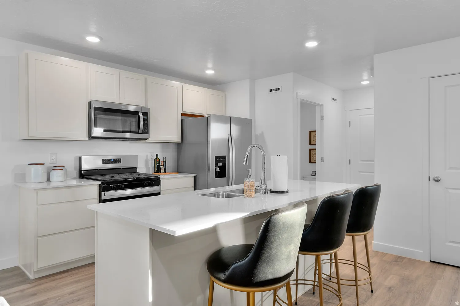 Kitchen featuring stainless steel appliances, light-toned cabinetry, a spacious island, integrated sink with gooseneck faucet, and wood-finish flooring