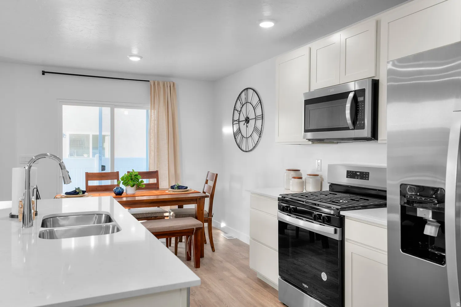 White kitchen cabinetry, stainless steel appliances, wood-finish flooring, recessed lighting, and a kitchen island with a double basin sink