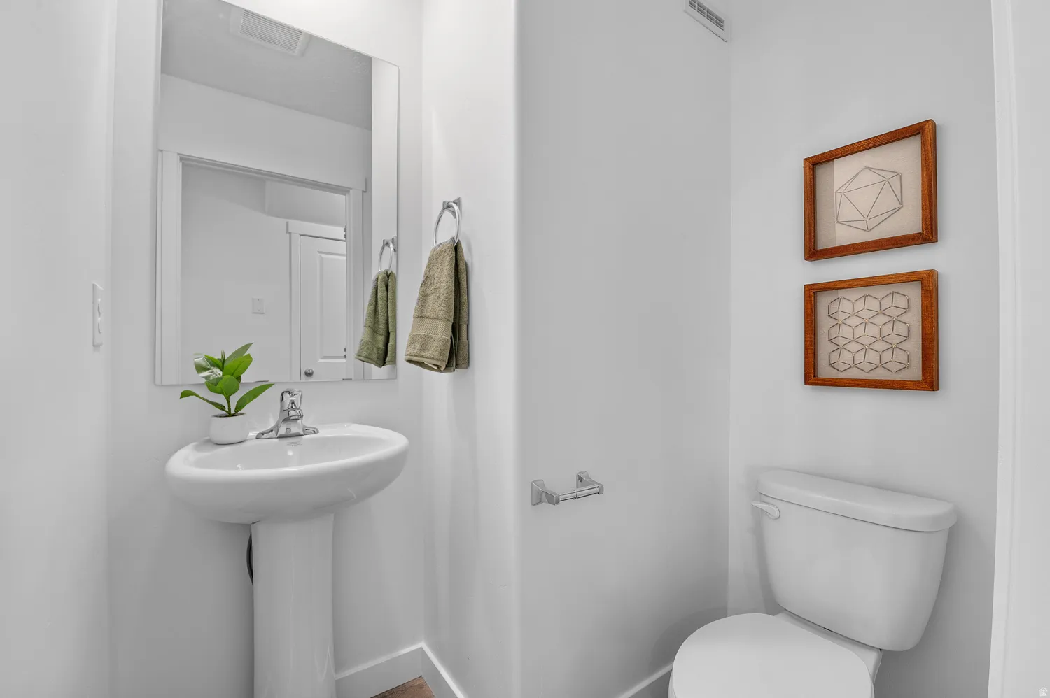 Pedestal sink with chrome faucet, wall-mounted mirror, and white toilet