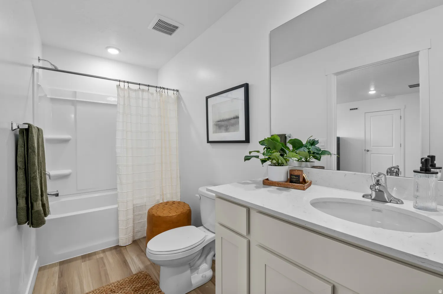 White vanity with a single basin and chrome faucet, large frameless mirror, and a built-in tub with shower