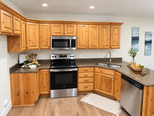 U-shaped kitchen with wood cabinetry, stainless steel appliances, speckled countertops, and wood-finish flooring