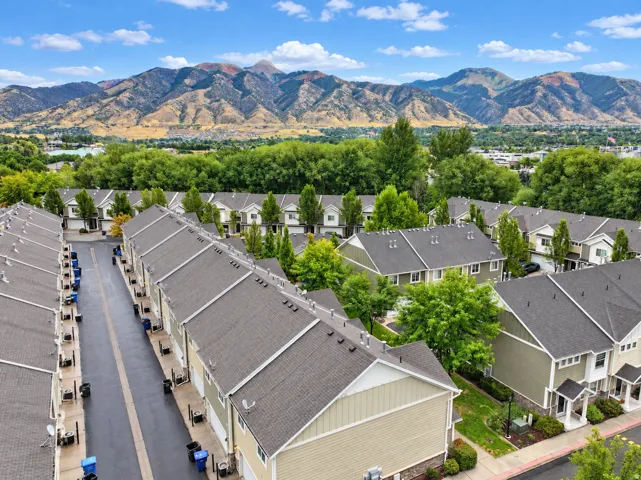 Mountain backdrop, residential development with multiple units, asphalt roadways, and mature trees