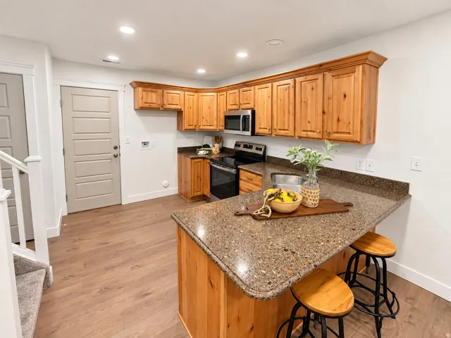 Corner kitchen featuring wood-finish cabinetry, stone-finish countertops, stainless steel appliances, and a central island with seating