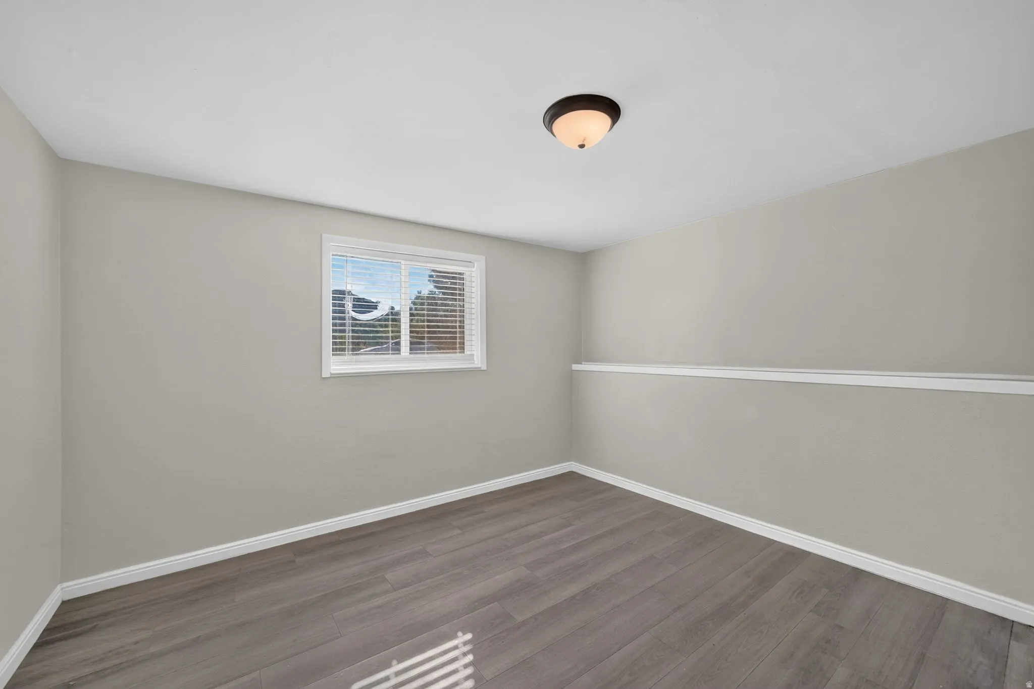 Neutral wall paint, wood-finish flooring, white trim, and a window with blinds