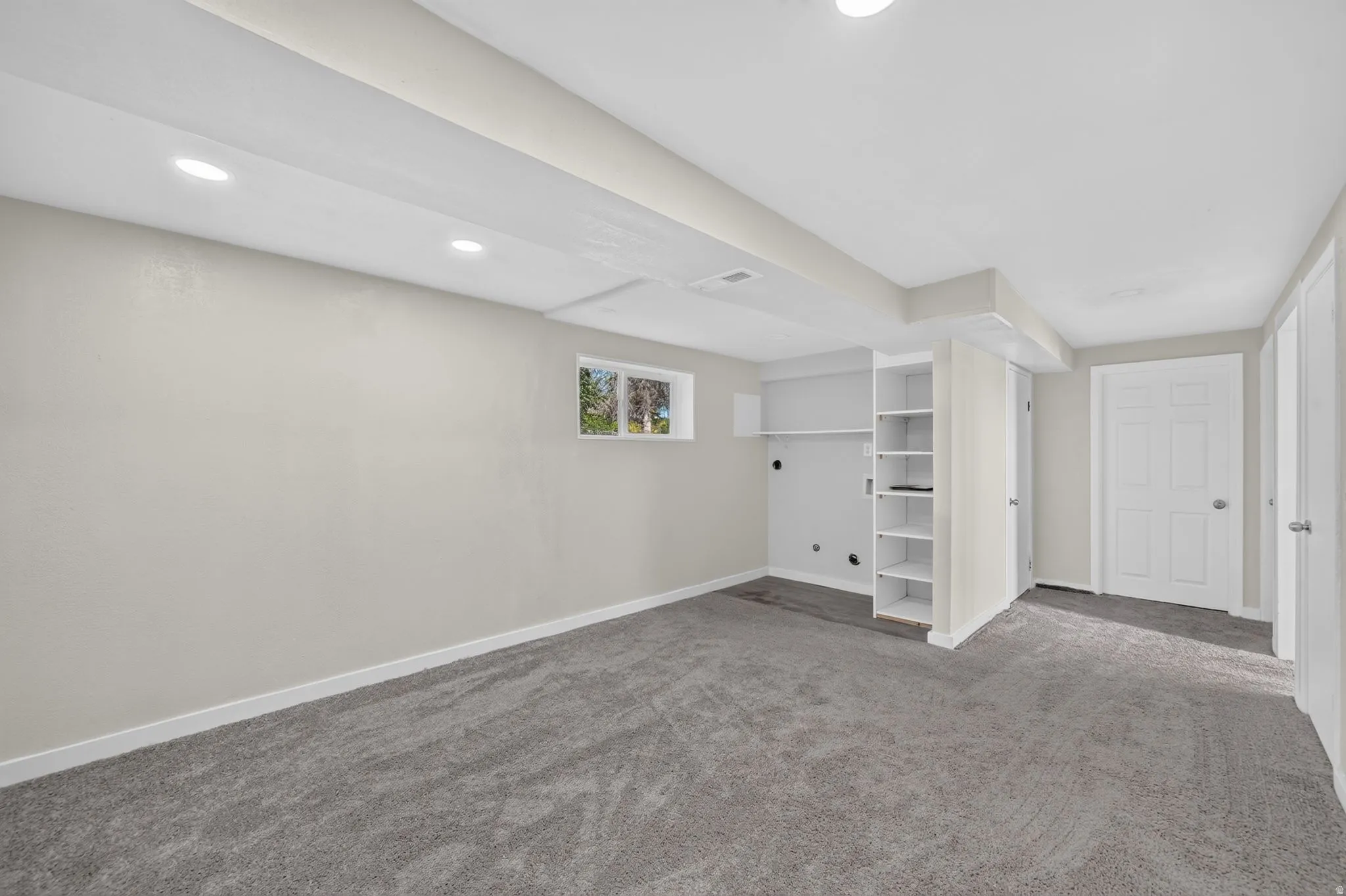 Recessed lighting, light gray wall finish, built-in shelving, gray carpeting, and a paneled door