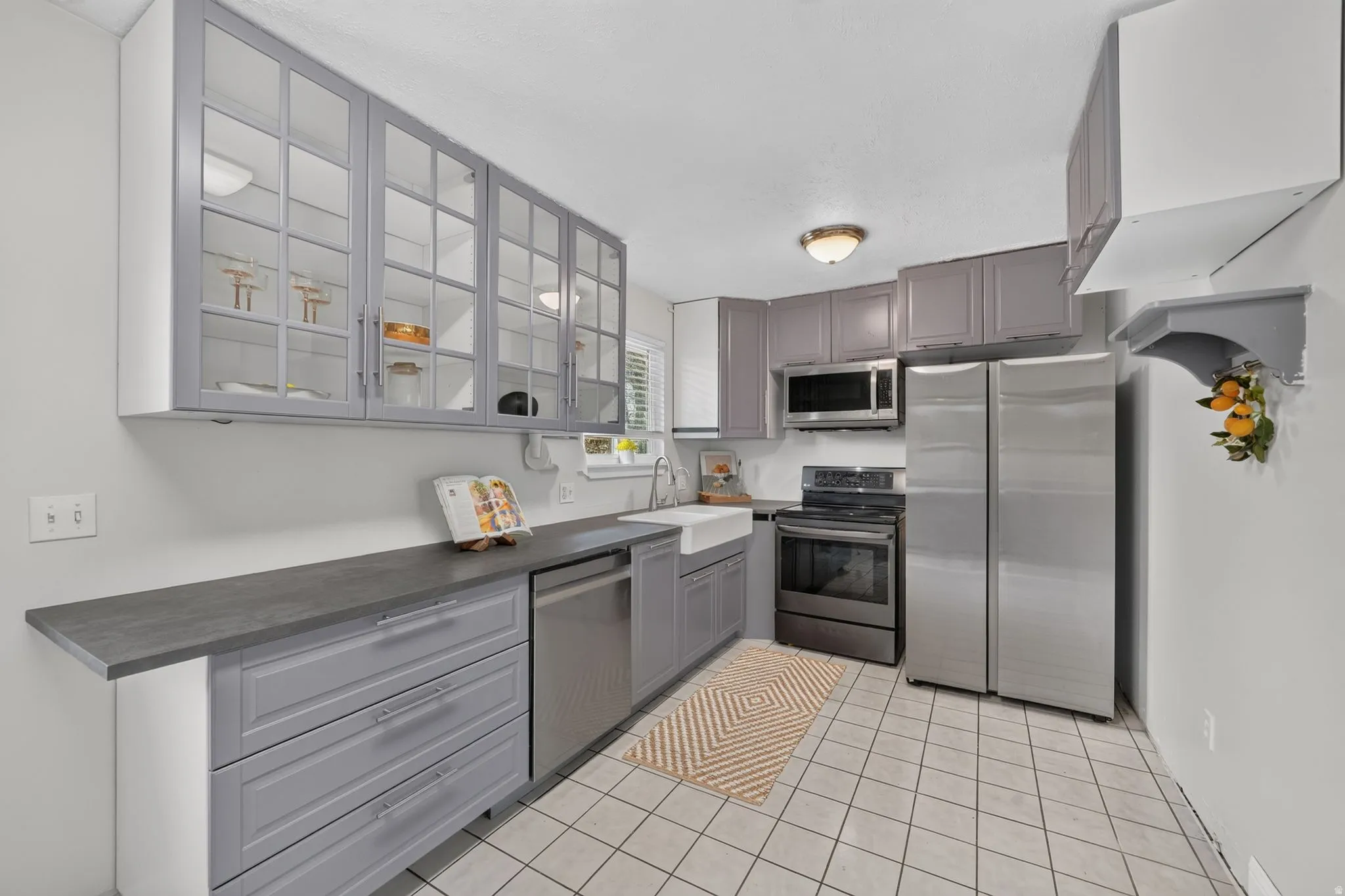 Kitchen featuring light gray cabinetry, stainless steel appliances, a farmhouse sink, and a tiled floor