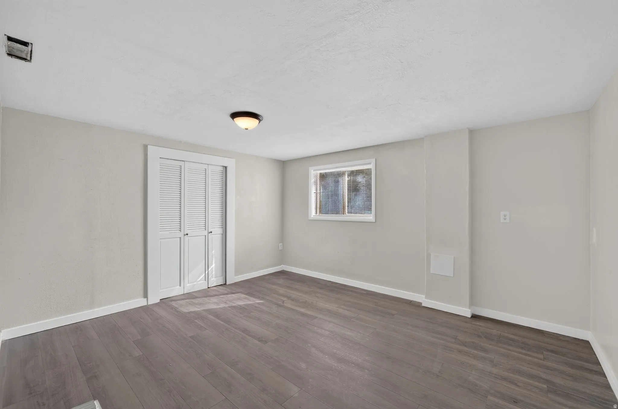 Wood-finish flooring, white bifold closet doors, and a window with white trim