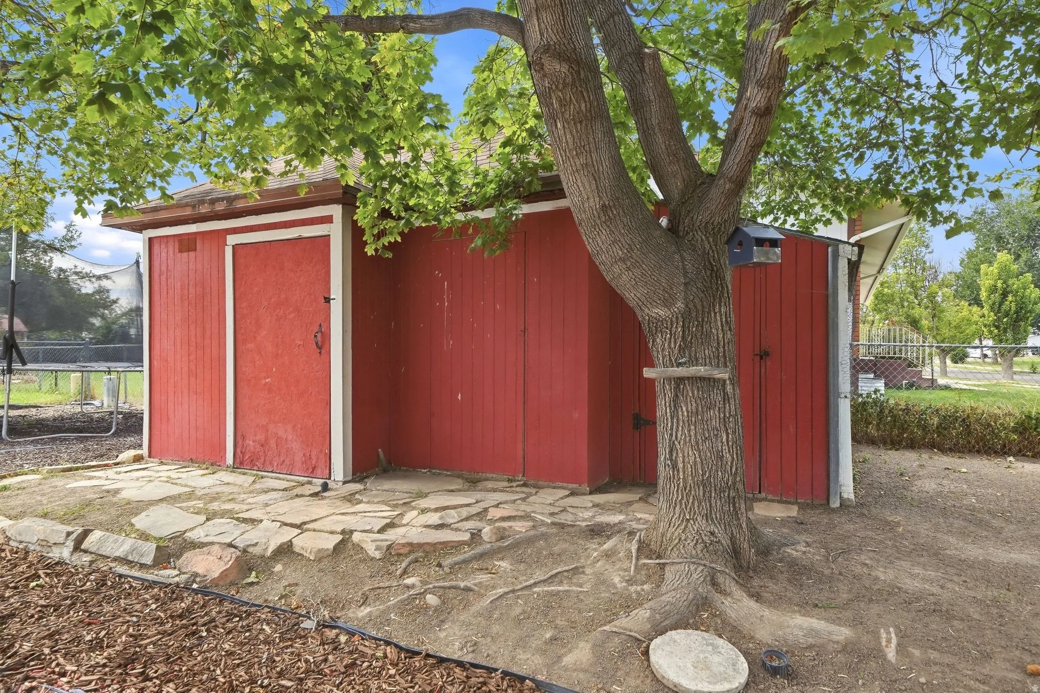 Red exterior shed with a single door, complemented by flagstone paving and an established tree