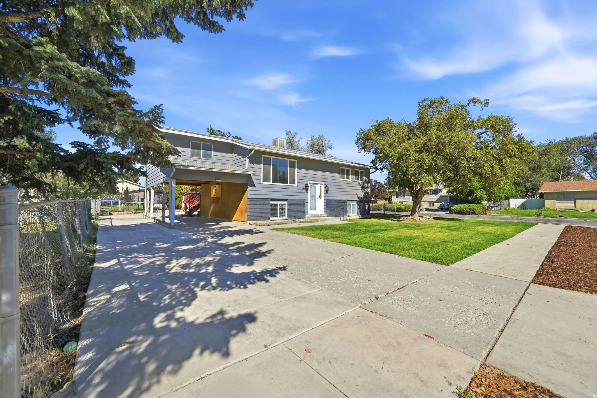 Split-level residence featuring gray siding, a covered carport, and a concrete driveway
