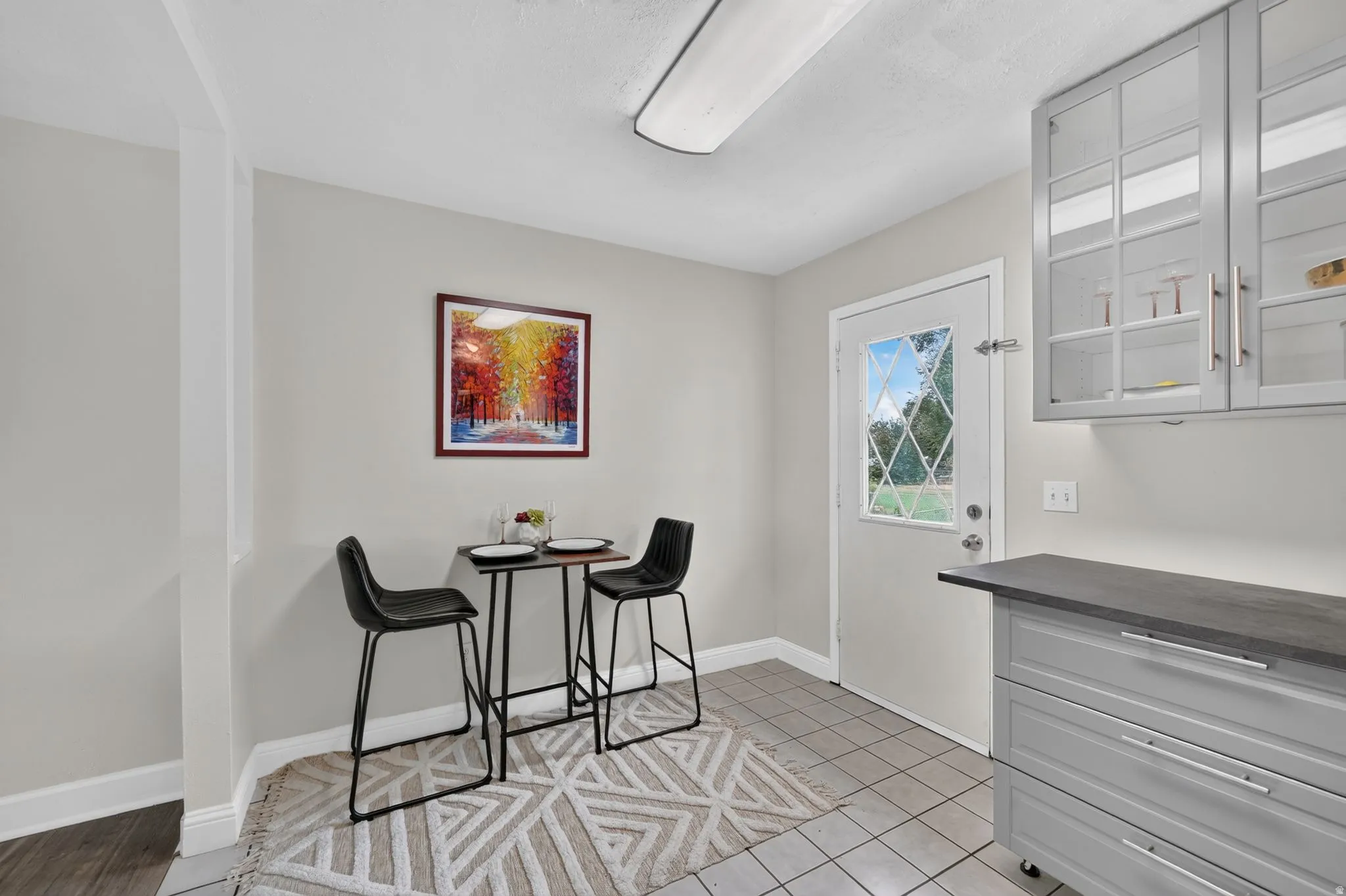Tile flooring, light gray cabinetry, glass-front upper cabinets, and a white exterior door with decorative lites