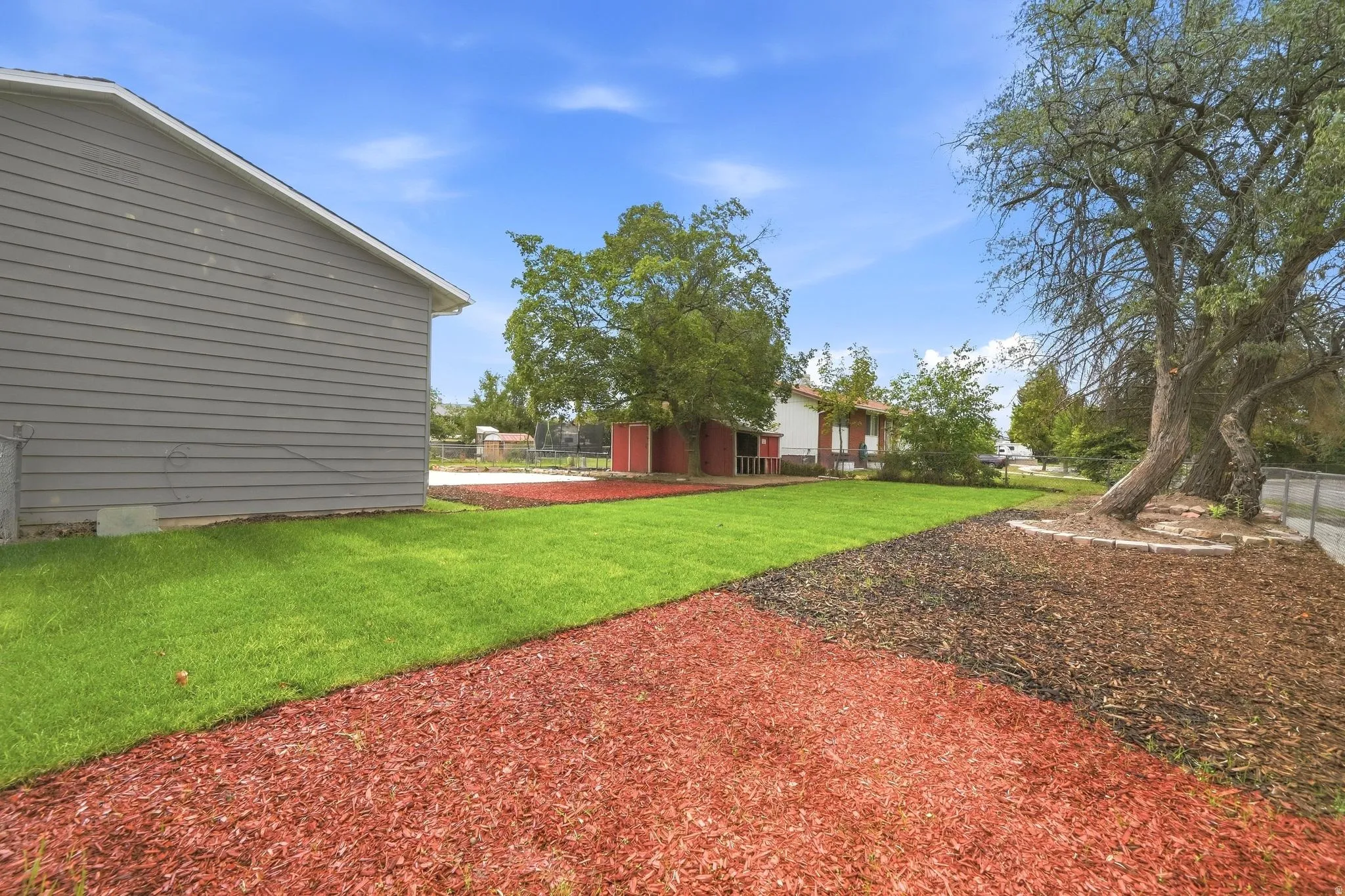 Expansive yard featuring a manicured lawn, red and brown mulch beds, and mature trees