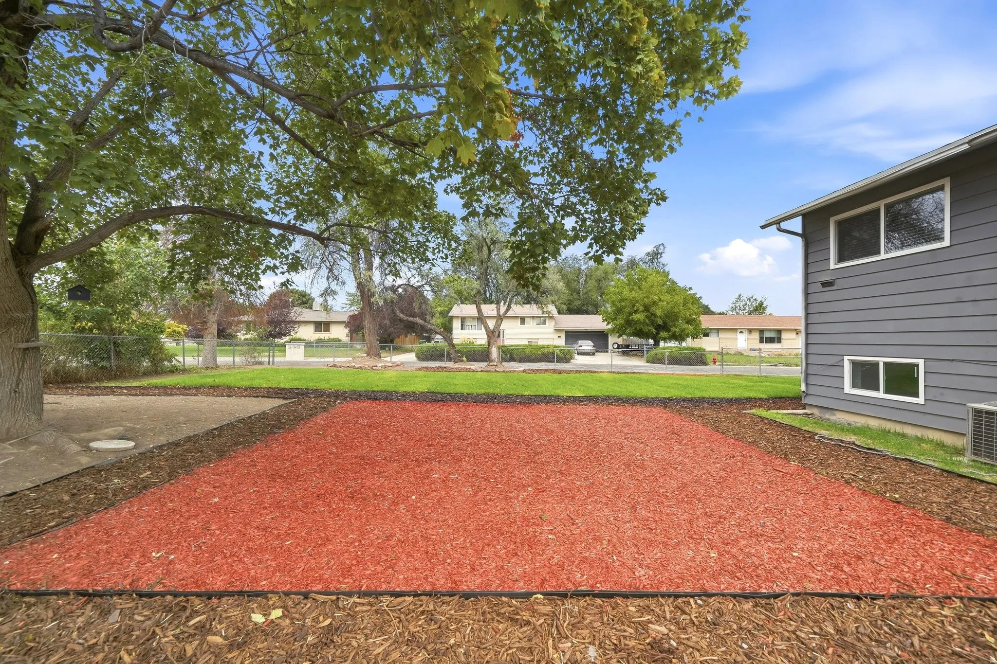Expansive yard featuring mature trees, a red bark area, and a dark brown mulch perimeter