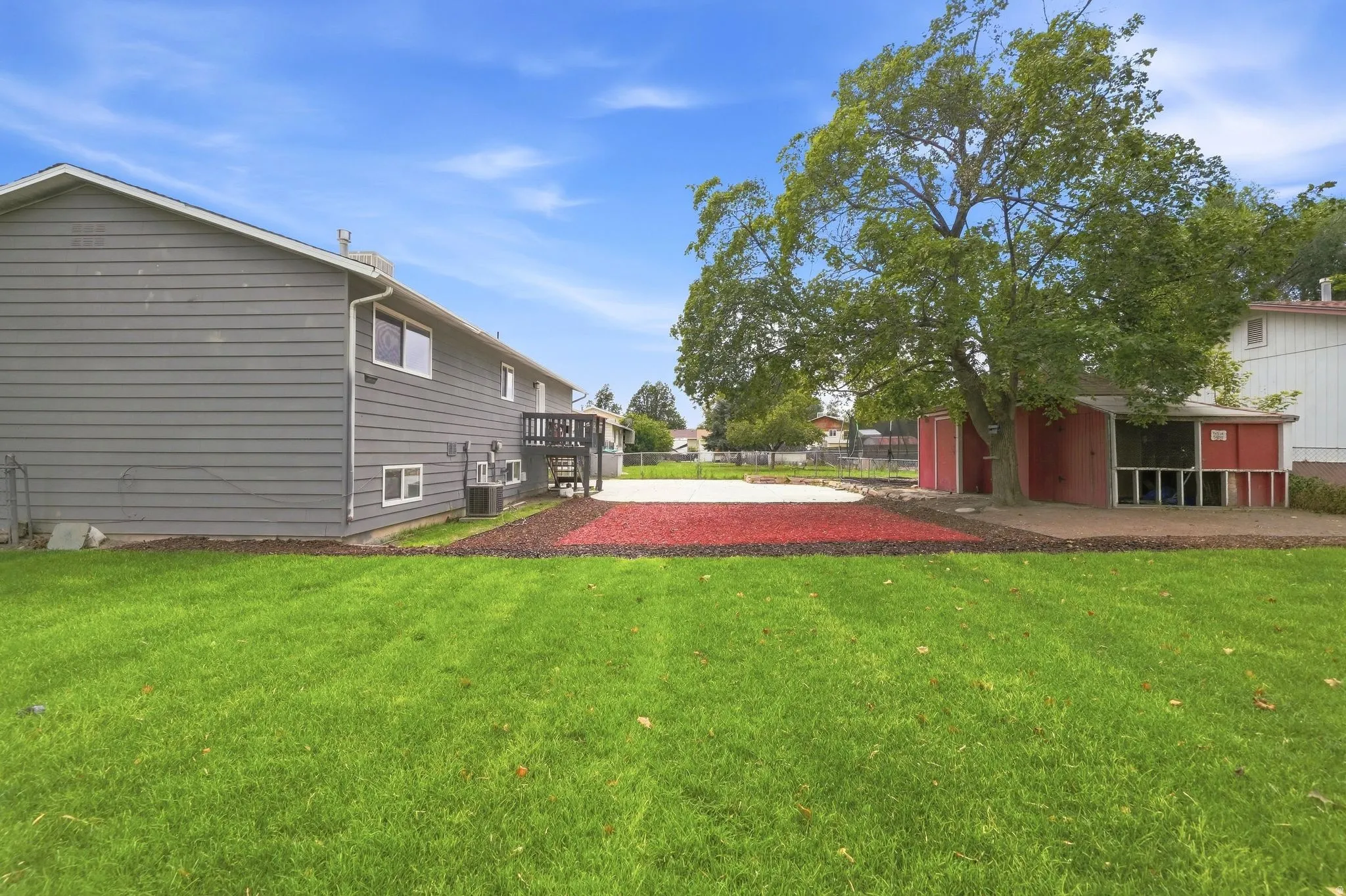 Expansive green lawn, concrete patio, mature tree, red mulch landscaping, and a detached shed structure