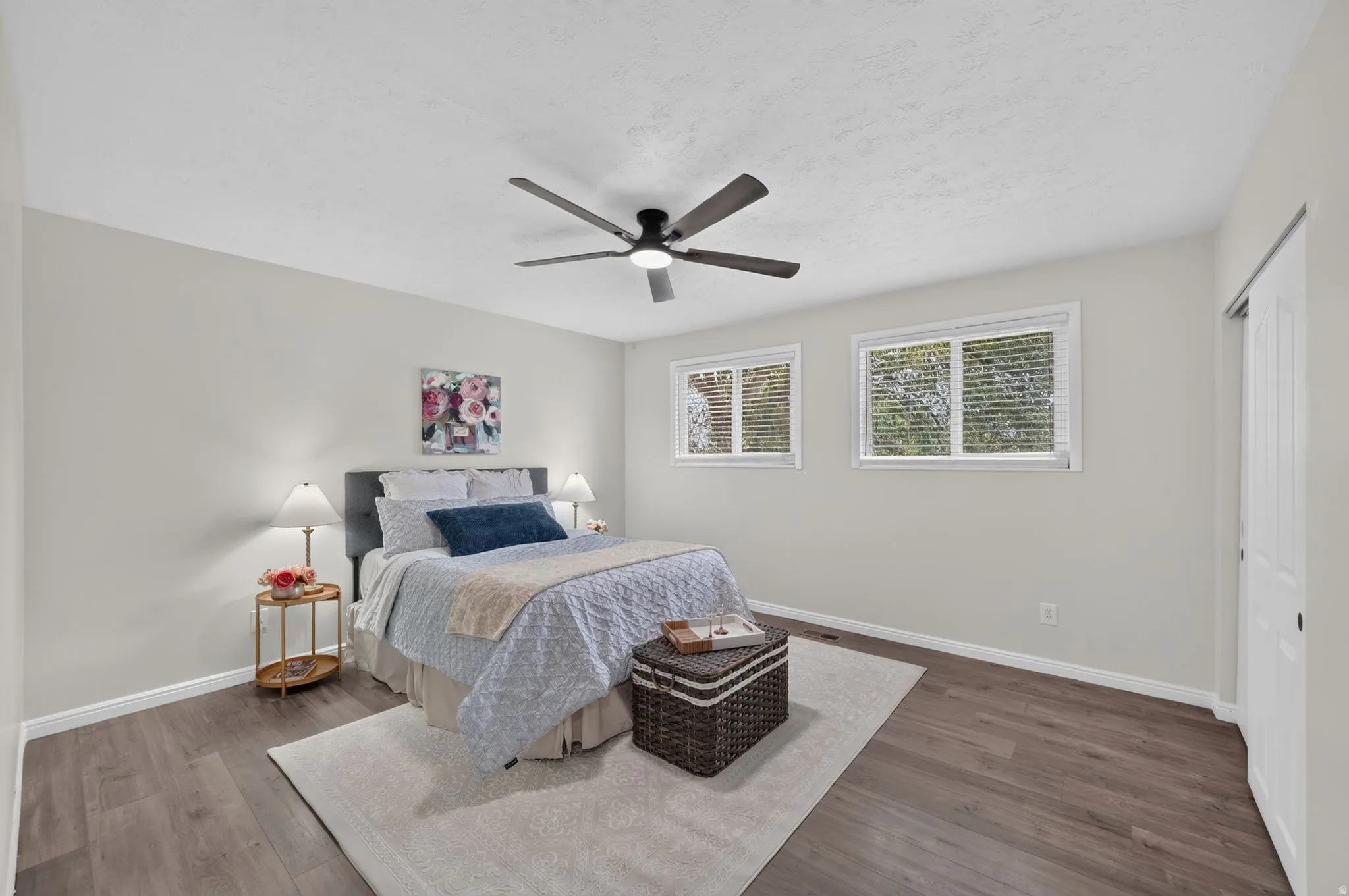 Wood-finish flooring, white walls, two windows, and a ceiling fan with integrated lighting