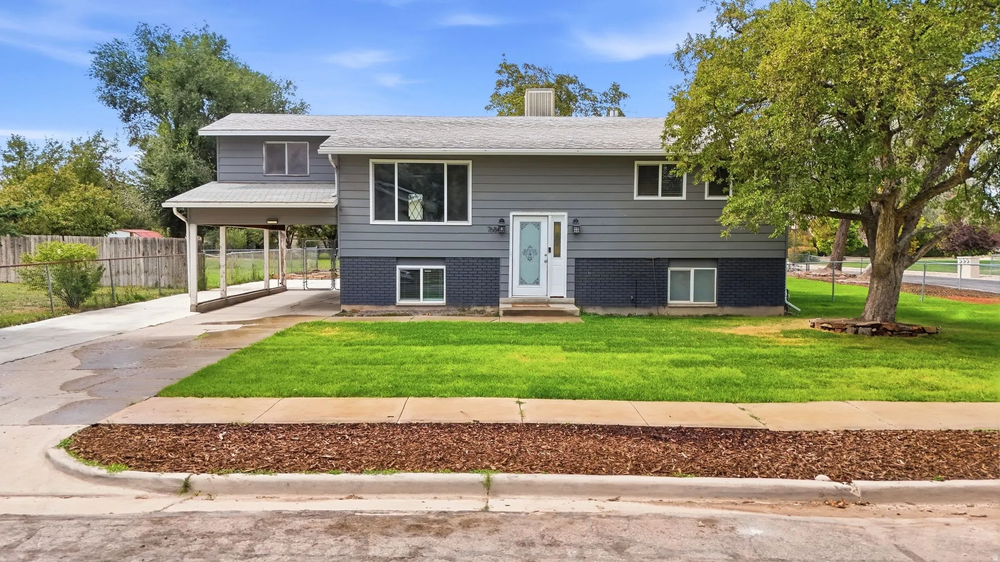 Split-level residence featuring a covered carport, a white entry door, and a gray siding exterior
