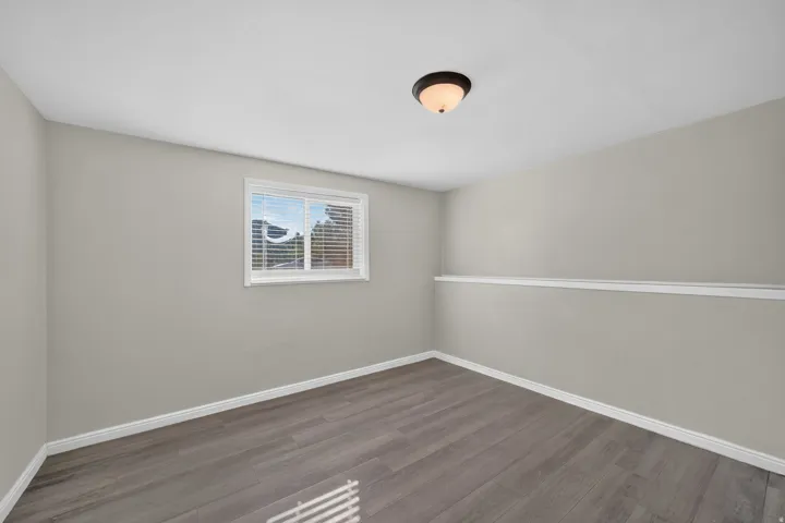Neutral wall paint, wood-finish flooring, white trim, and a window with blinds
