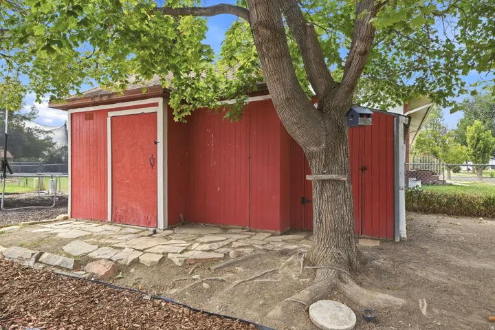 Red exterior shed with a single door, complemented by flagstone paving and an established tree