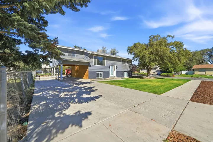 Split-level residence featuring gray siding, a covered carport, and a concrete driveway