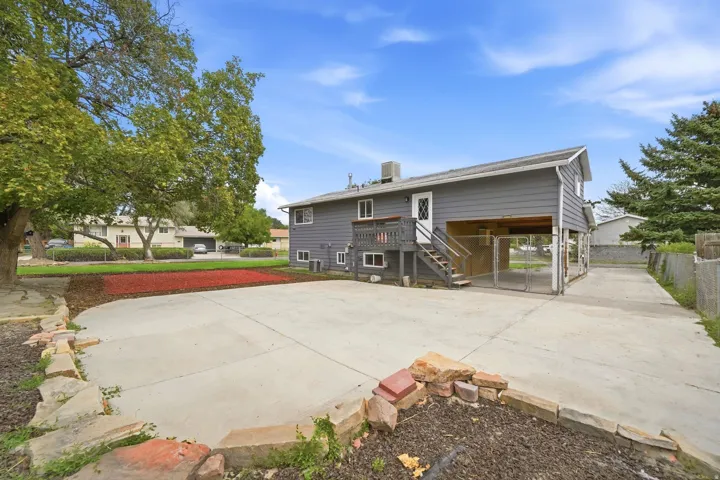 Gray siding exterior with white trim, elevated wood deck with stairs, concrete driveway, and established trees
