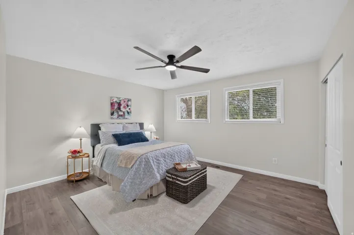 Wood-finish flooring, white walls, two windows, and a ceiling fan with integrated lighting