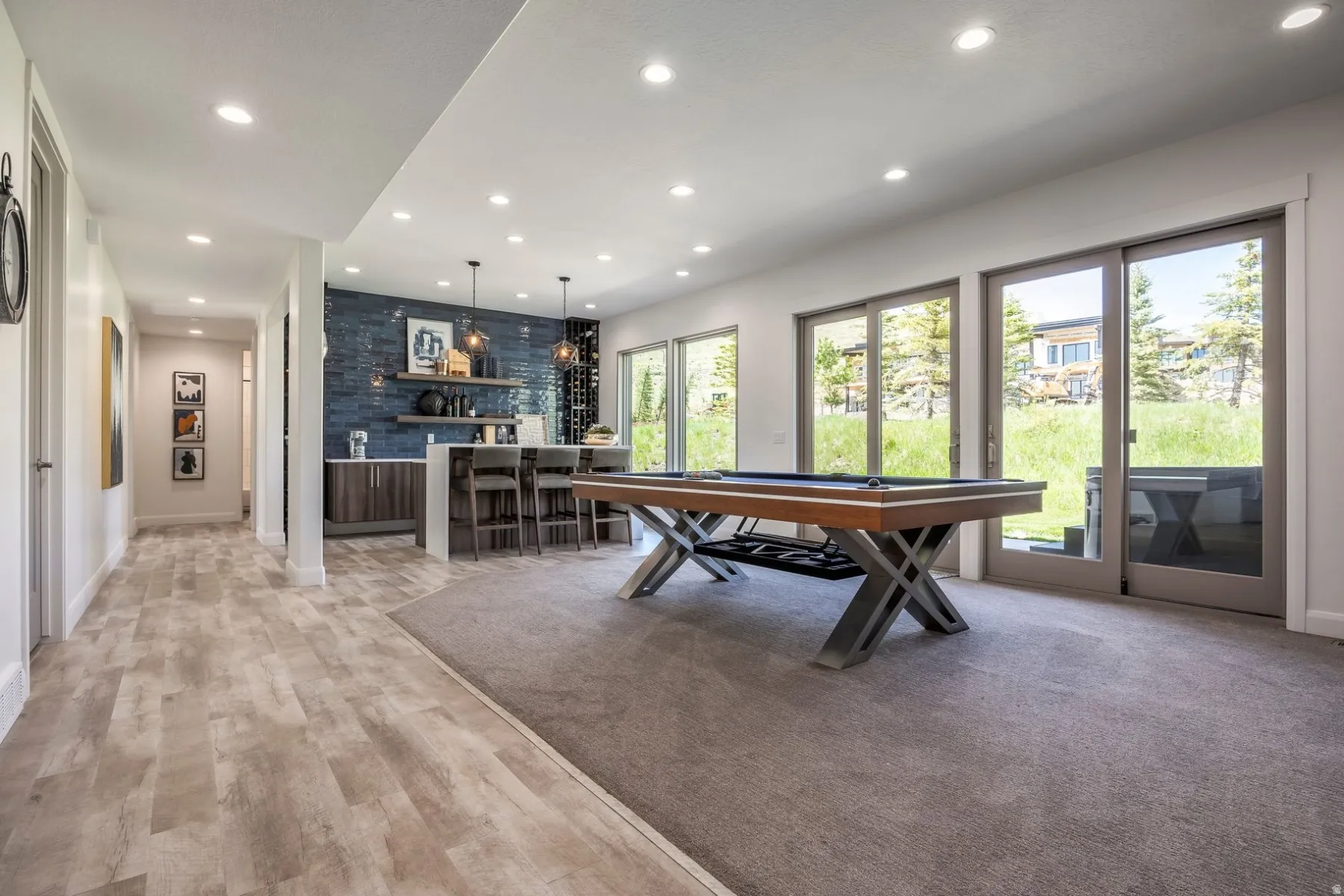 Recessed lighting, wood-finish flooring, built-in wet bar with a tiled accent wall, built-in wine storage, and multiple sliding glass doors