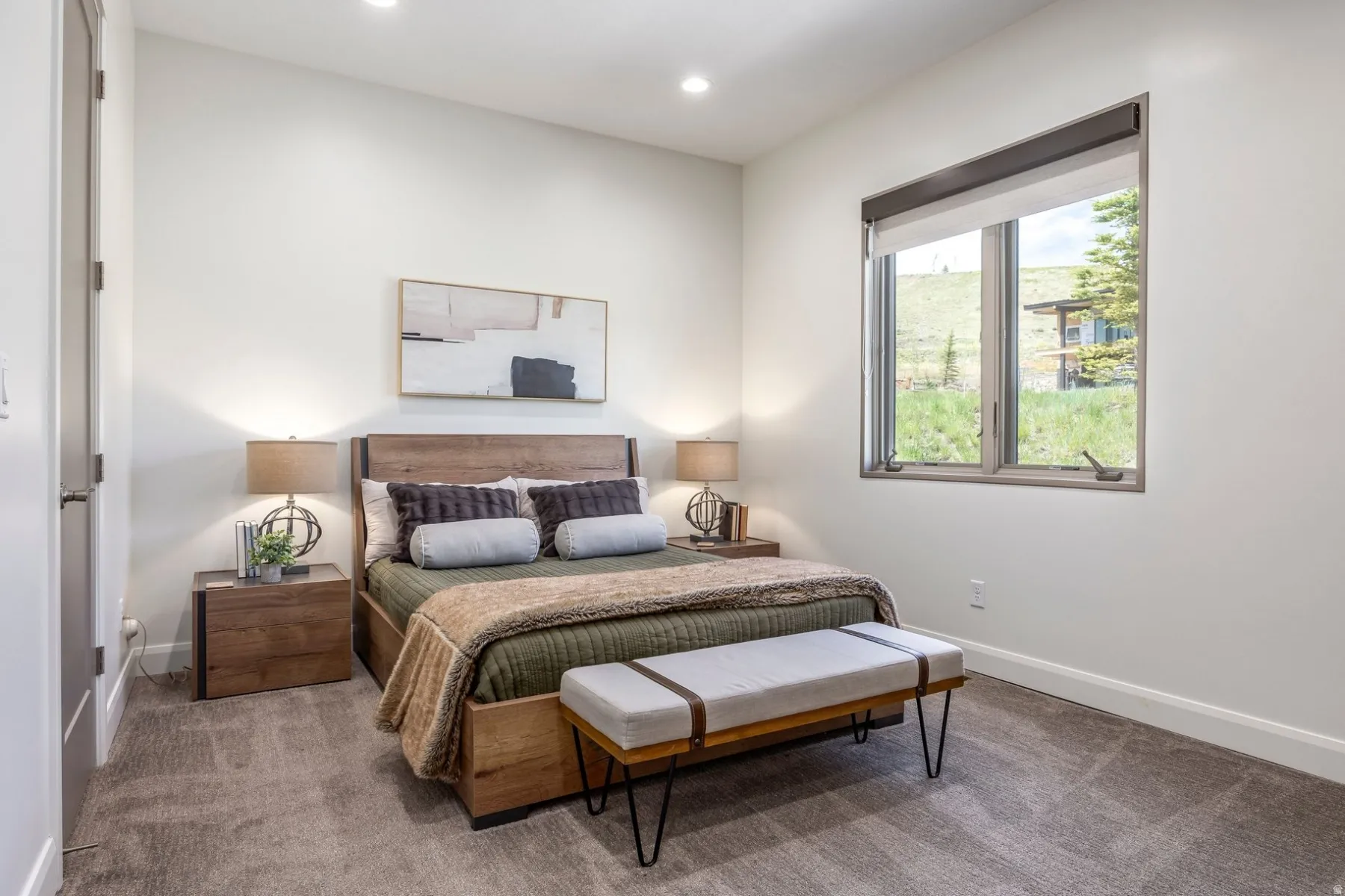 Recessed lighting, wood-finish bed frame, wood-finish nightstands, soft gray carpeting, and a large window
