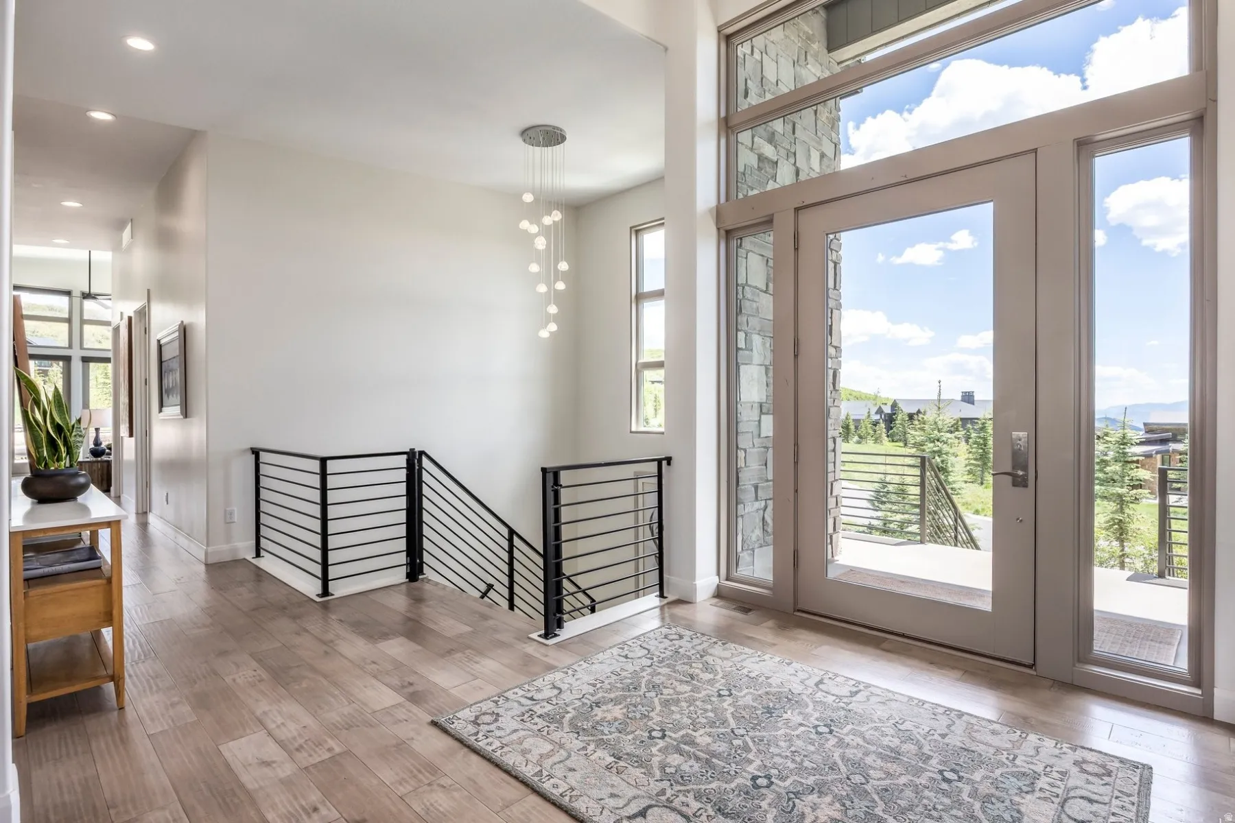 Entry with wood-finish flooring, a modern chandelier, and a metal horizontal bar railing
