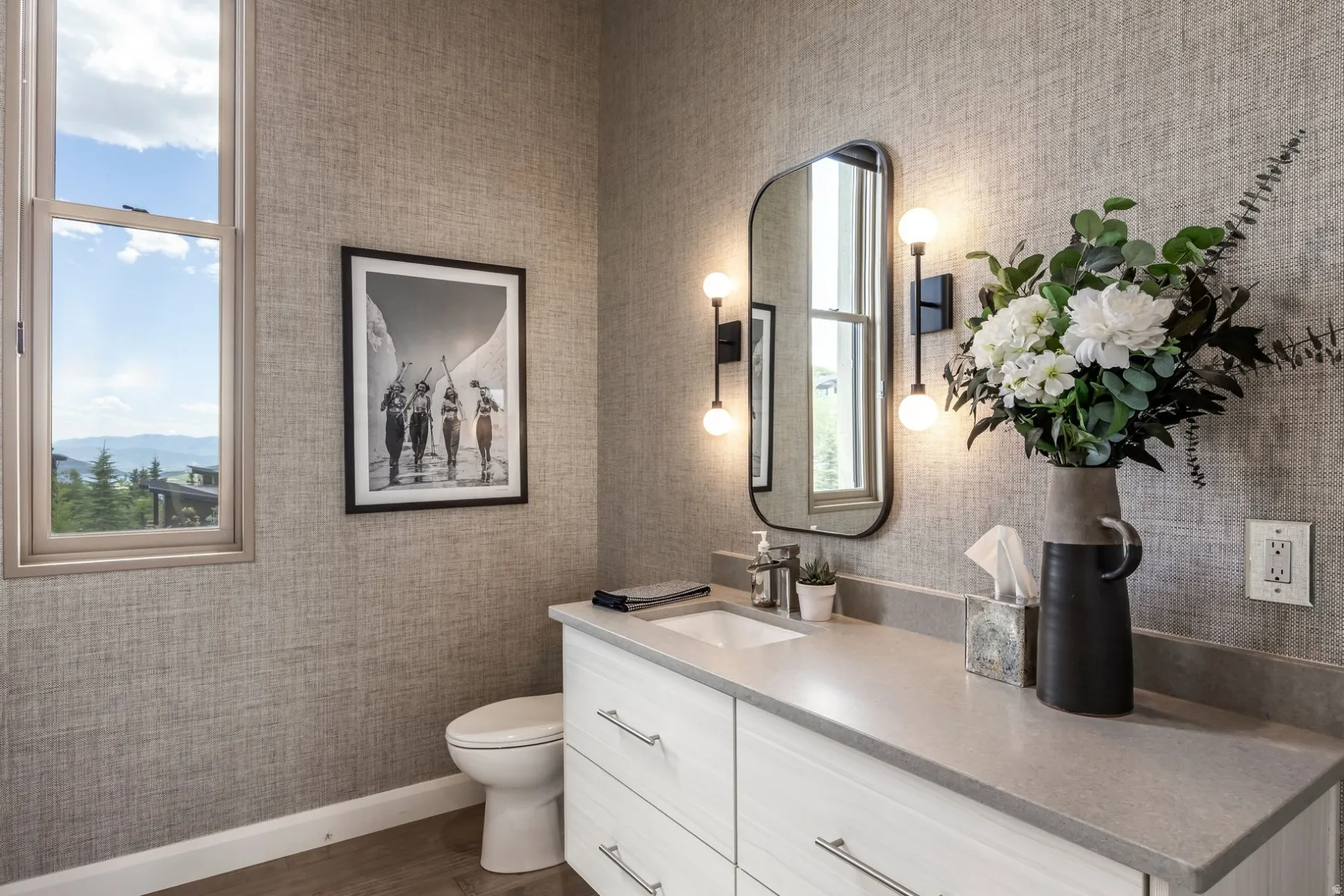 Single basin vanity with light-toned countertop, framed mirror, and wall-mounted lighting fixtures