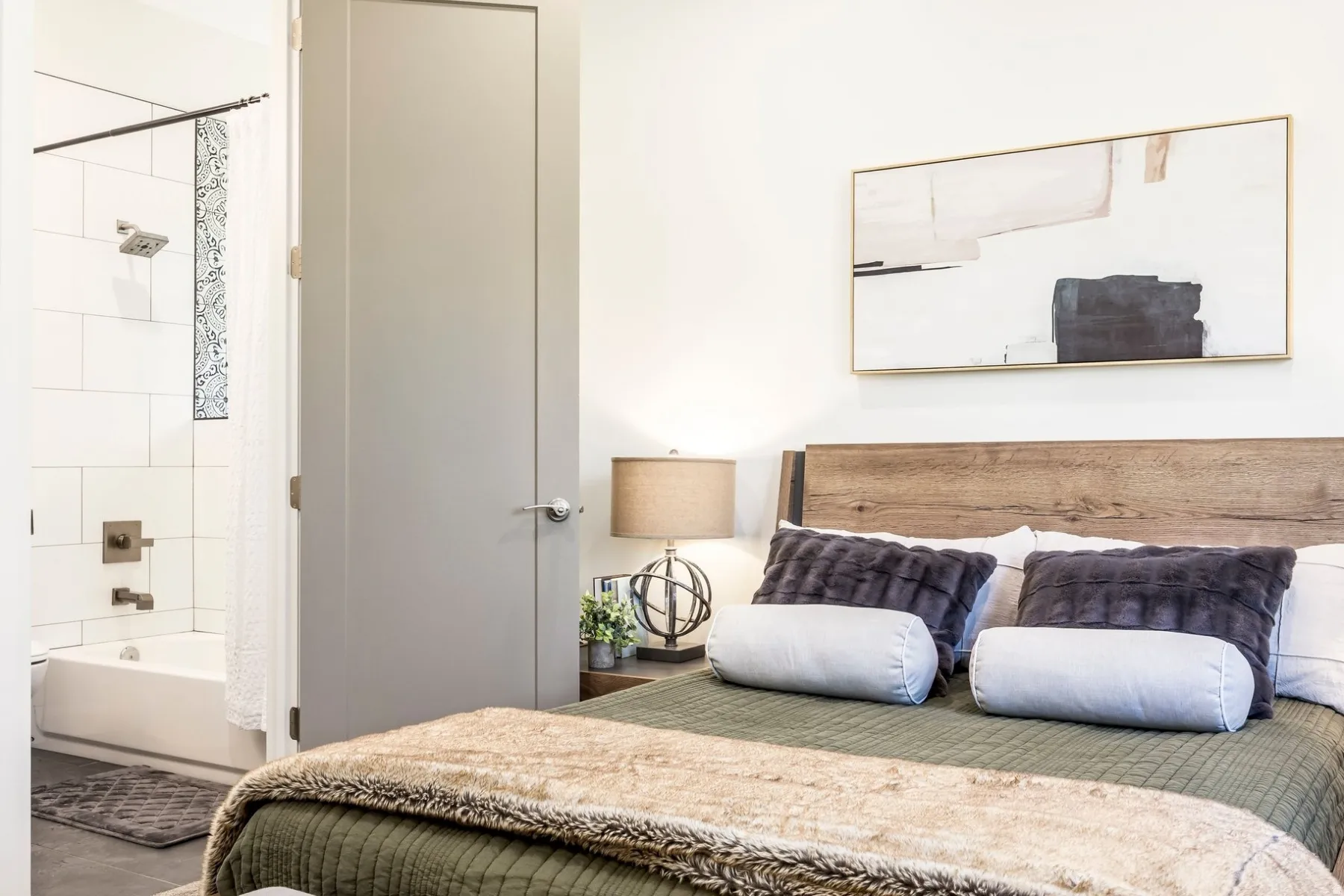 Warm wood-finish headboard, modern flat-panel door, and a full bathroom with white subway tile