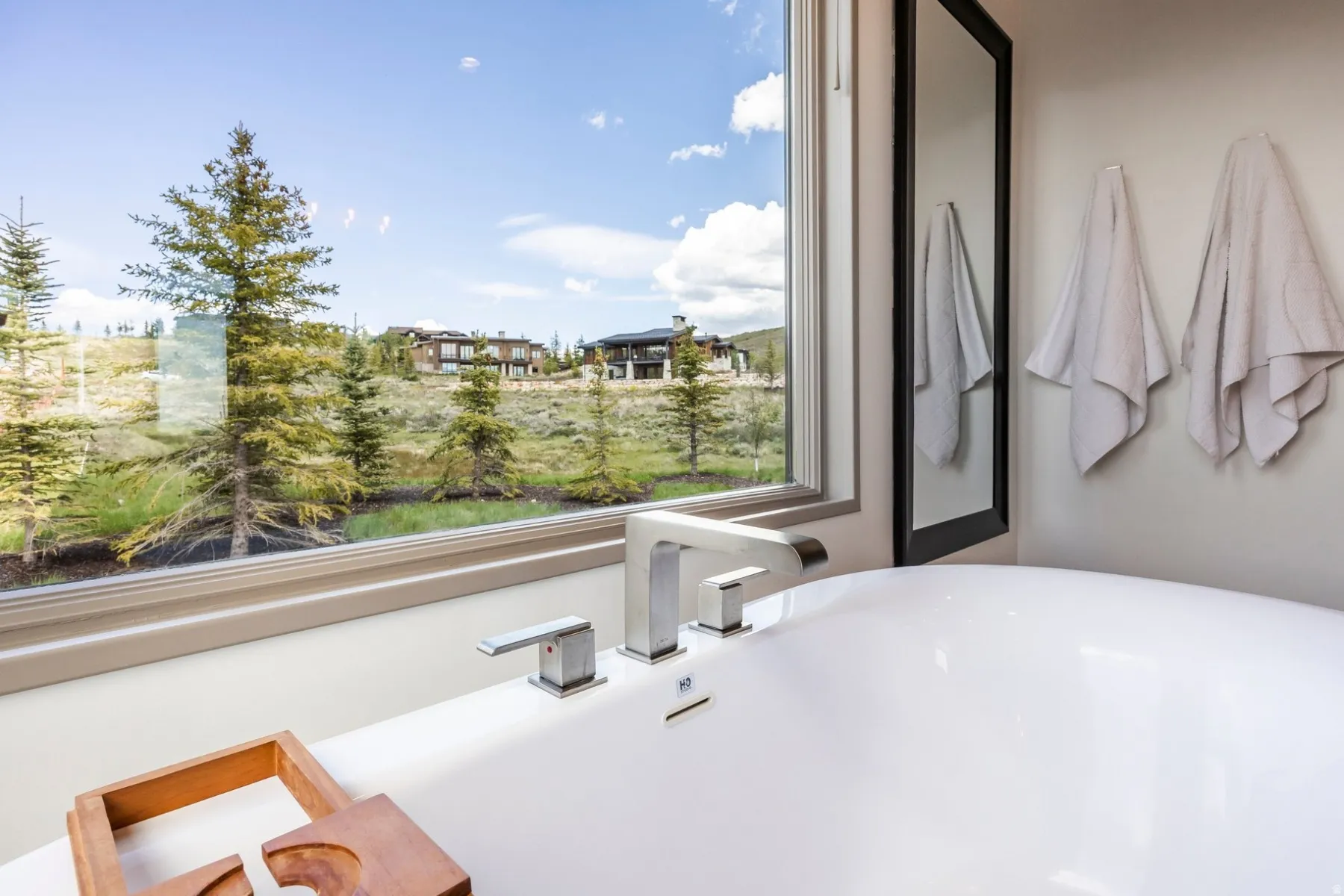 Freestanding soaking tub with polished chrome fixtures, oversized window, and natural surroundings