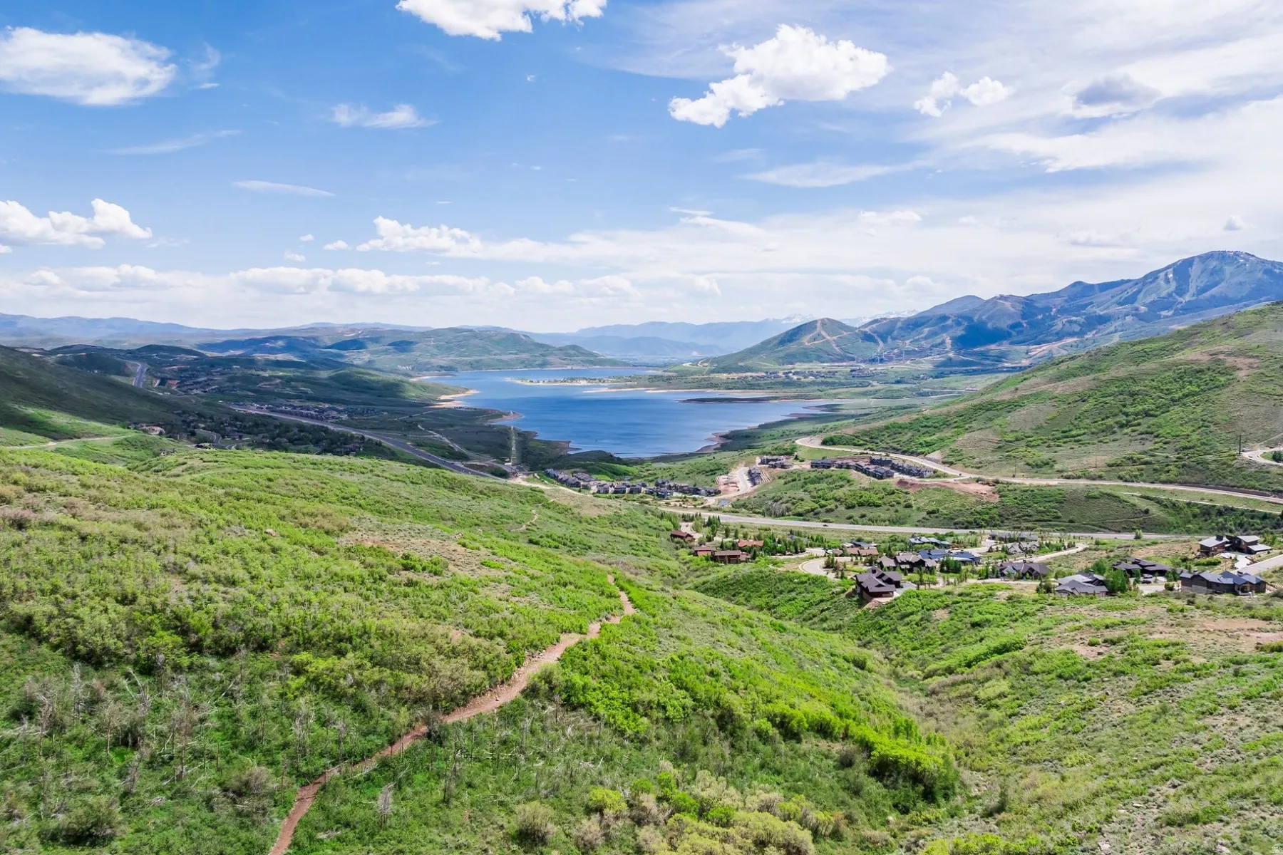 Expansive mountain landscape featuring a large body of water, green hillsides, and distant residences