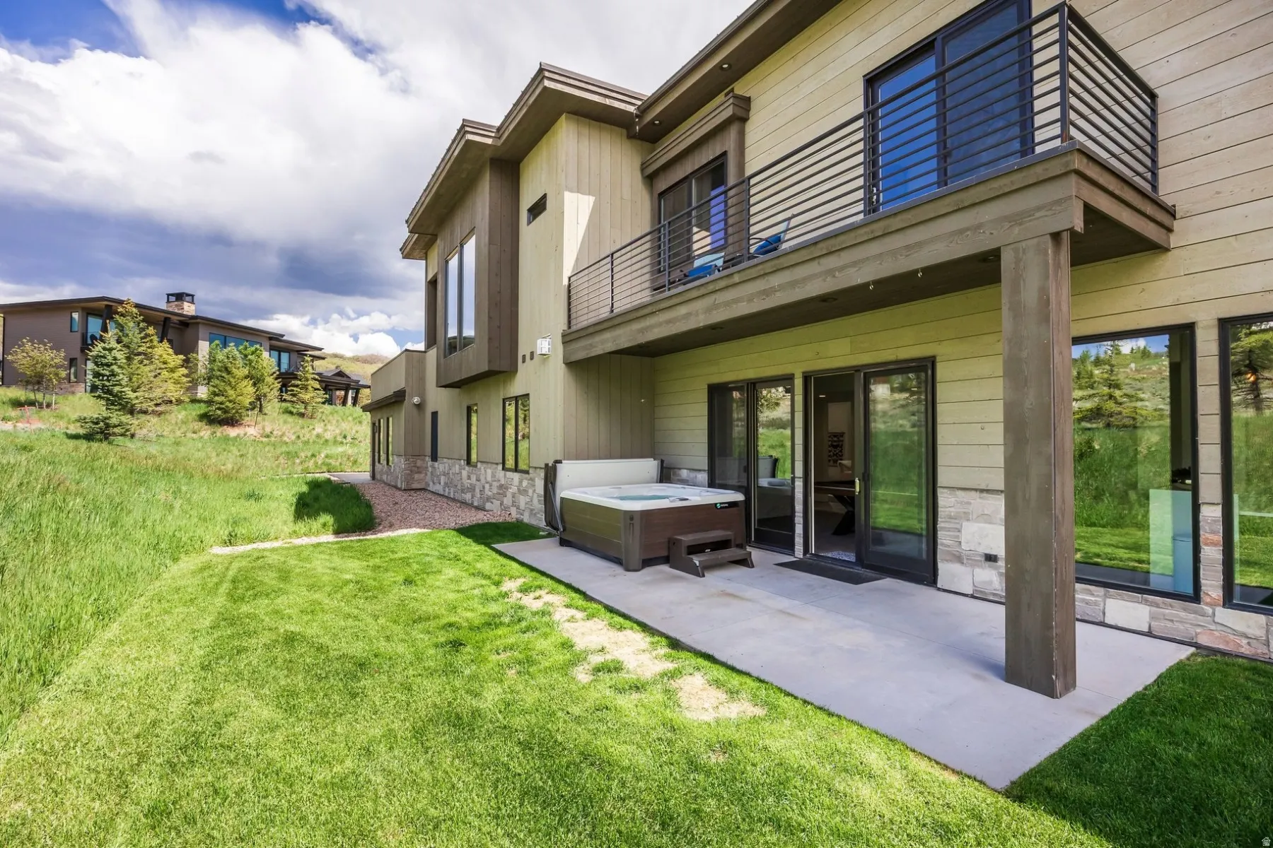 Rear exterior featuring a ground-level patio, upper-level balcony with horizontal railings, and an integrated hot tub