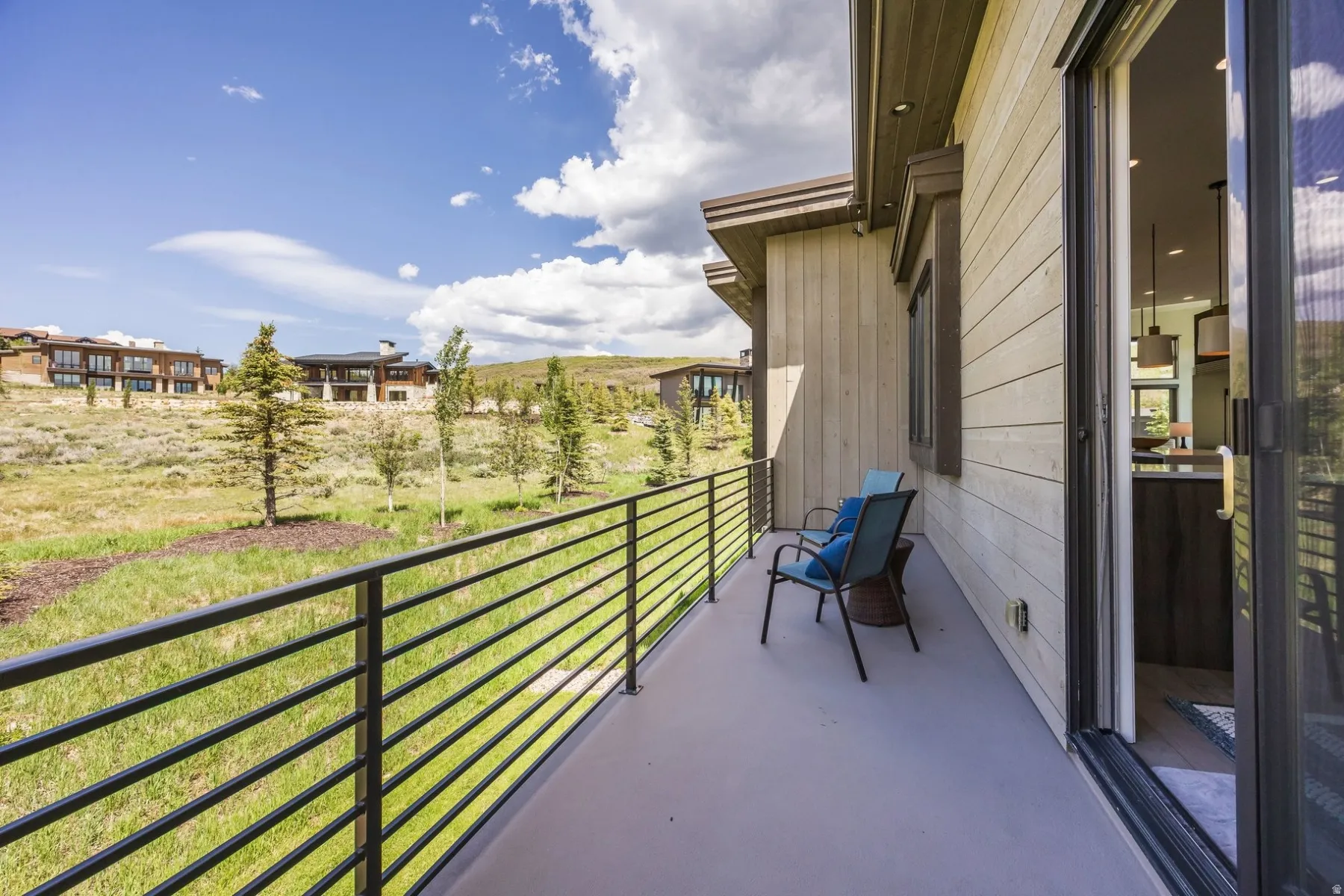 Expansive outdoor patio with metal railing, sliding glass door, and wooden exterior siding