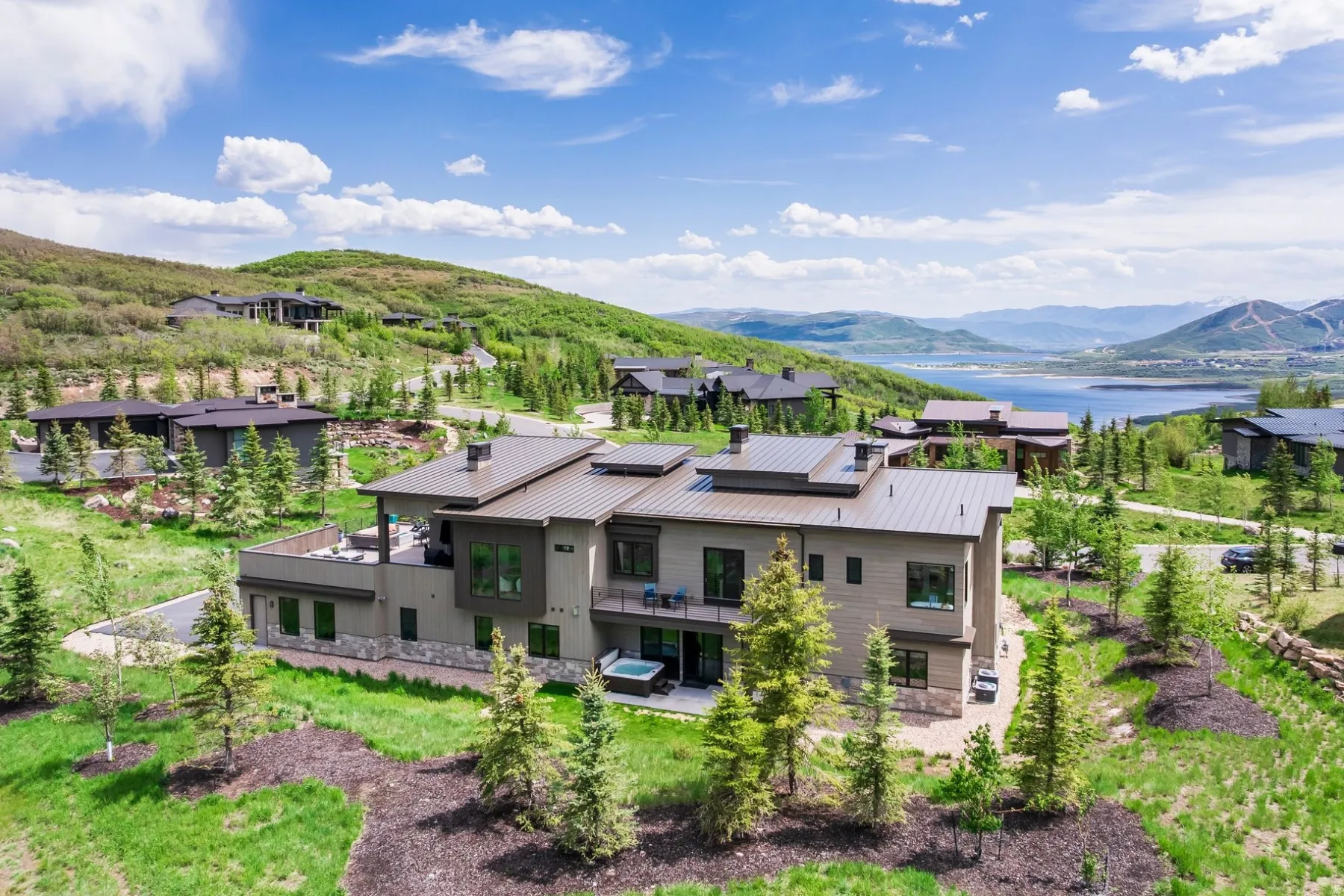 Modern multi-level exterior with extensive windows, multiple balconies, a ground-level patio, and an integrated hot tub