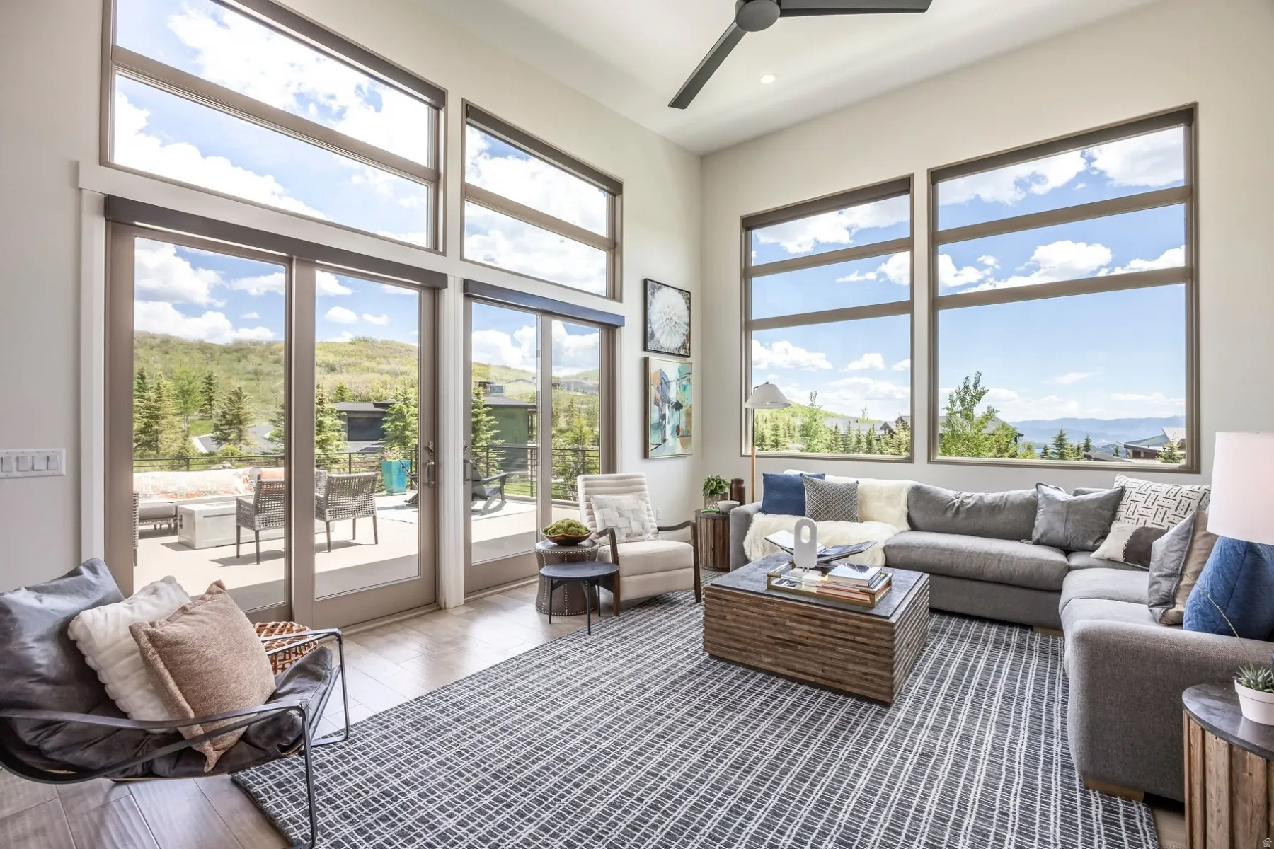 Expansive floor-to-ceiling windows, soaring ceiling height, wood-finish flooring, and a contemporary ceiling fan