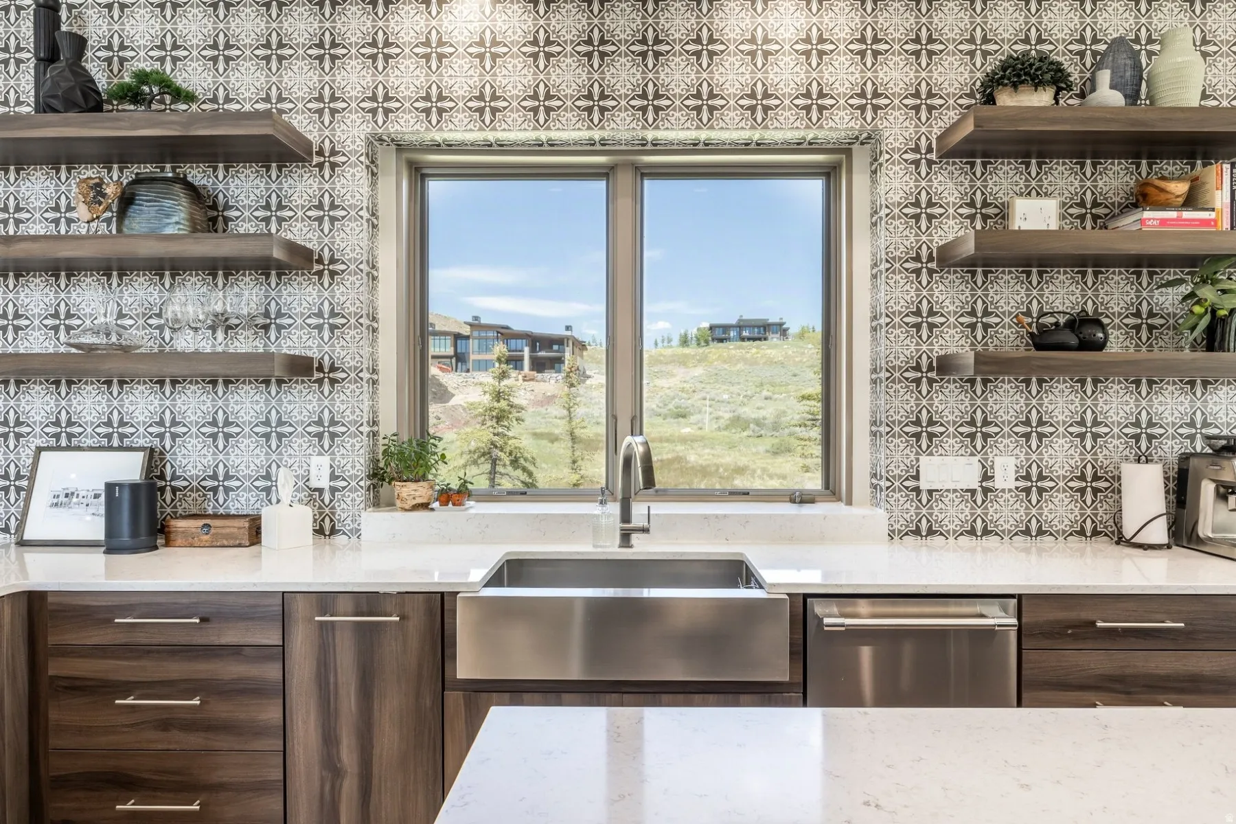 Patterned tile backsplash, floating wood-finish shelves, under-mount stainless steel sink, stainless steel dishwasher, and light-toned countertops