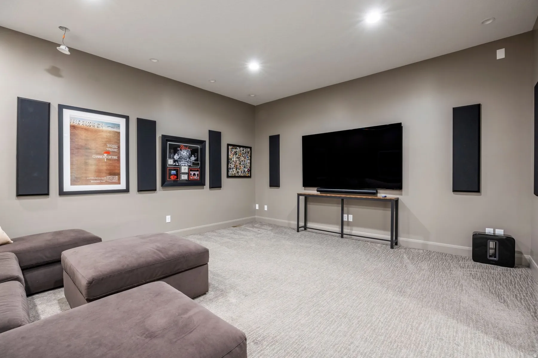 Recessed ceiling lighting, wall-mounted sound panels, light-colored patterned carpeting, and a console table with a wood-finish top