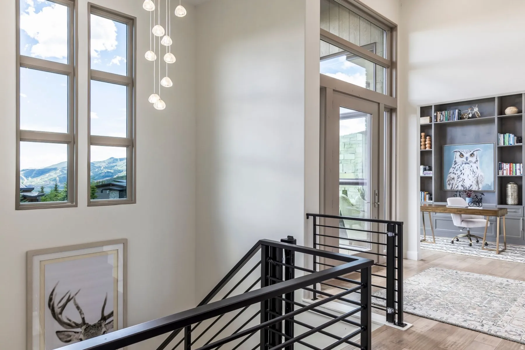 Double-height entry with a multi-pane window, suspended light fixture, black metal railing, and wood-finish flooring