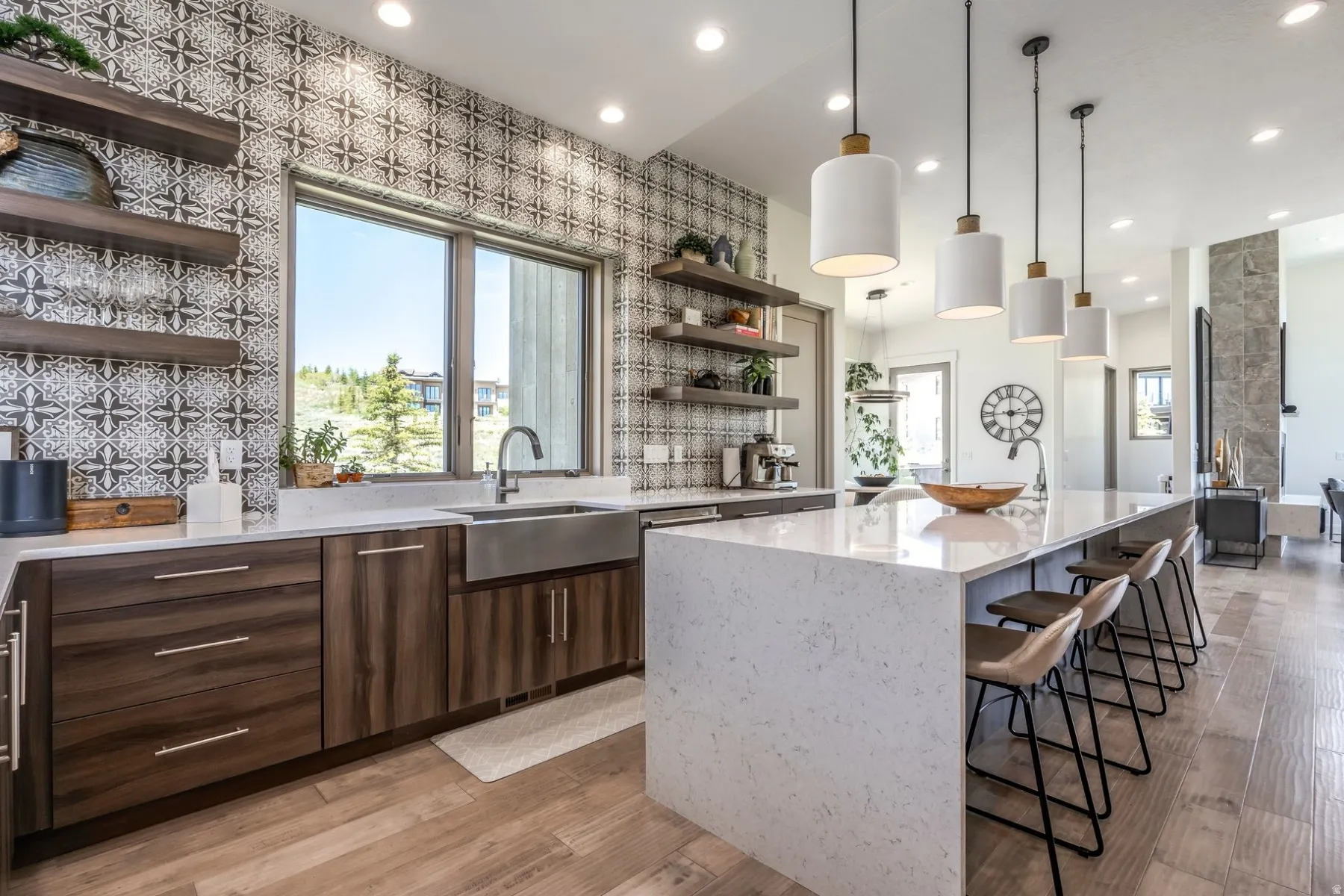 Custom tile accent wall, wood-finish flooring, built-in open shelving, stainless steel farmhouse sink, and a large center island with integrated seating