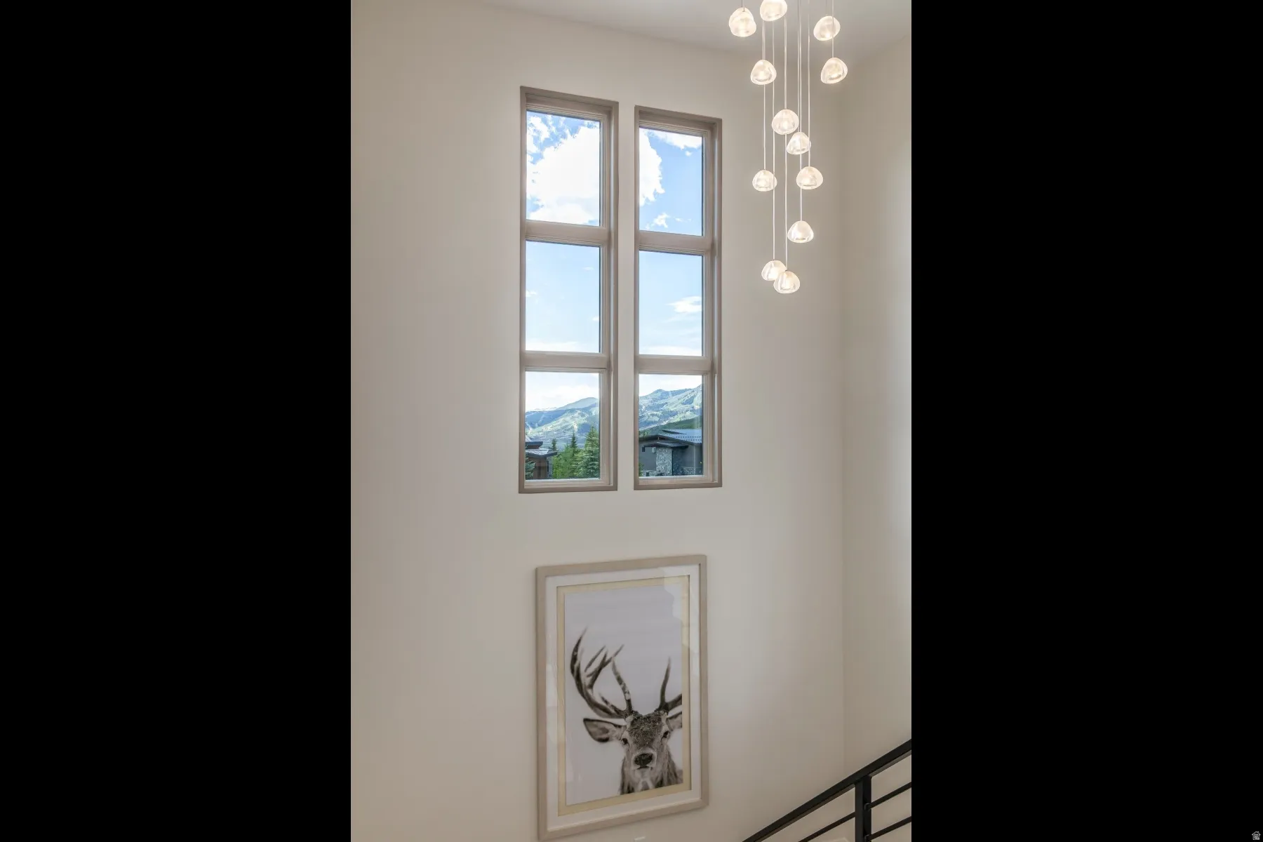 Soaring vertical windows, multi-pane window design, contemporary chandelier with multiple pendants, mountain scenery