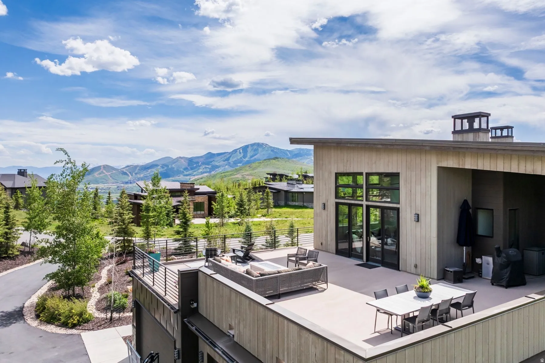 Expansive exterior deck, mountain backdrop, flat roofline, floor-to-ceiling windows, and multiple outdoor lighting fixtures