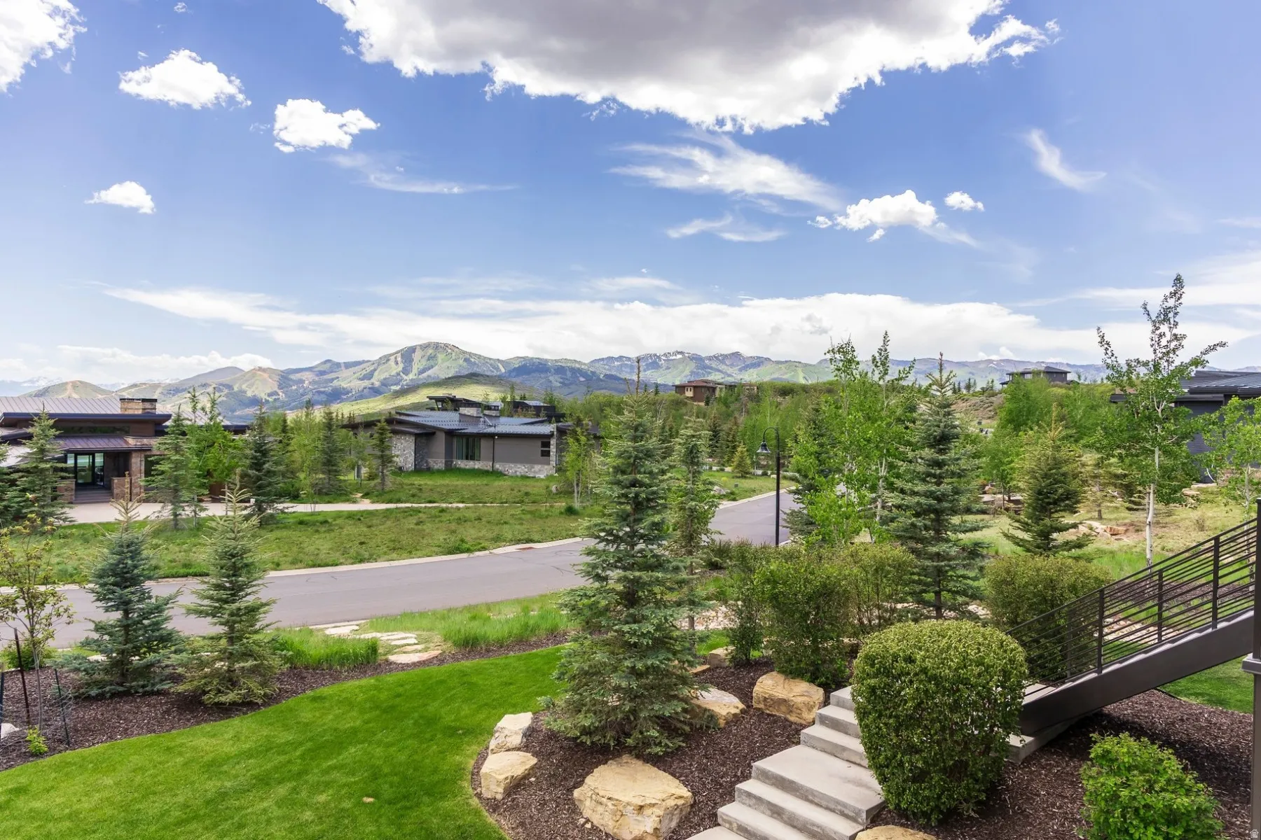 Expansive mountain scenery, manicured lawn, established landscaping, concrete steps, and modern exterior stairs with metal railings