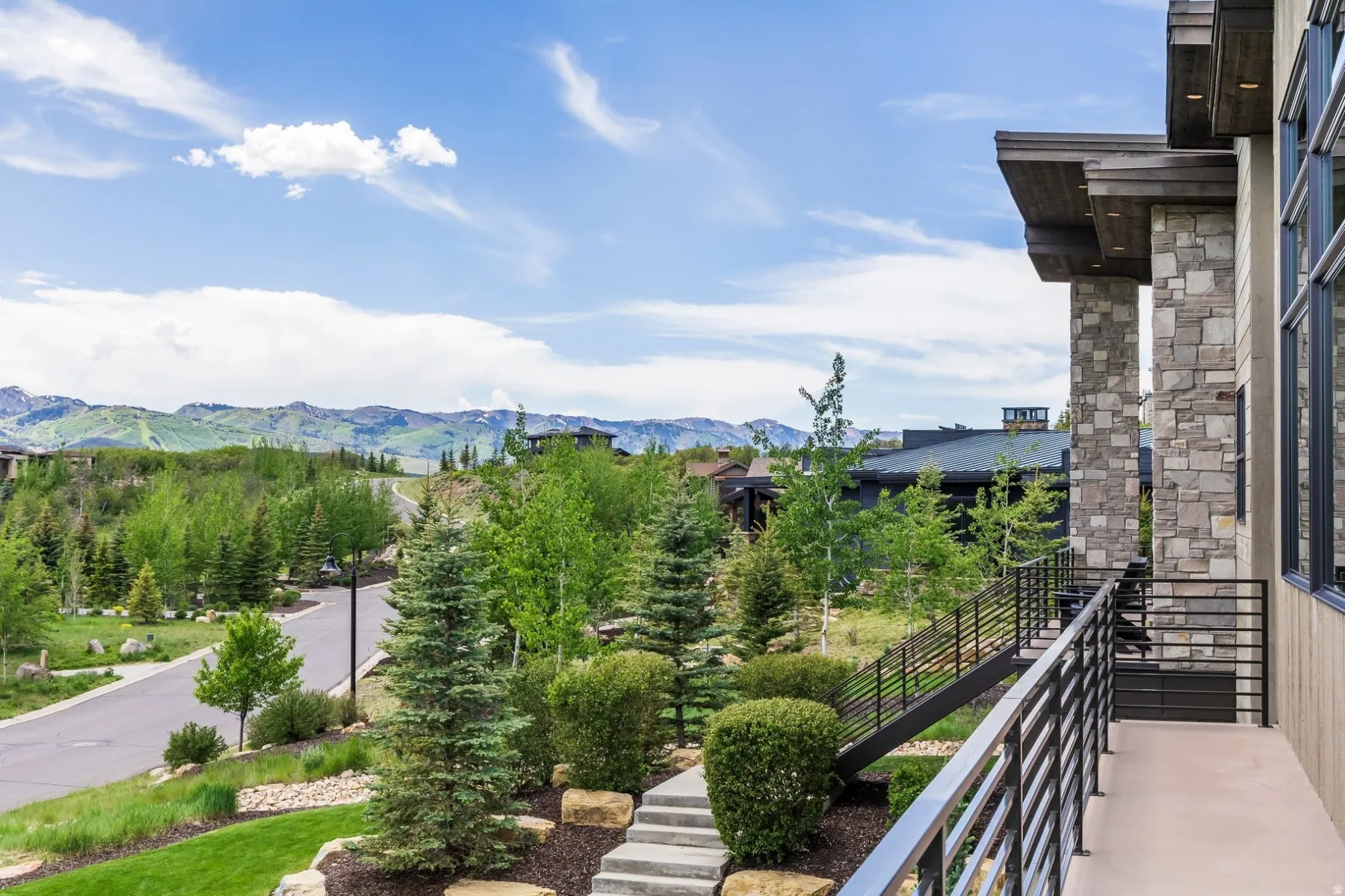 Stone and wood-clad exterior with expansive windows, a concrete balcony, and horizontal metal railings