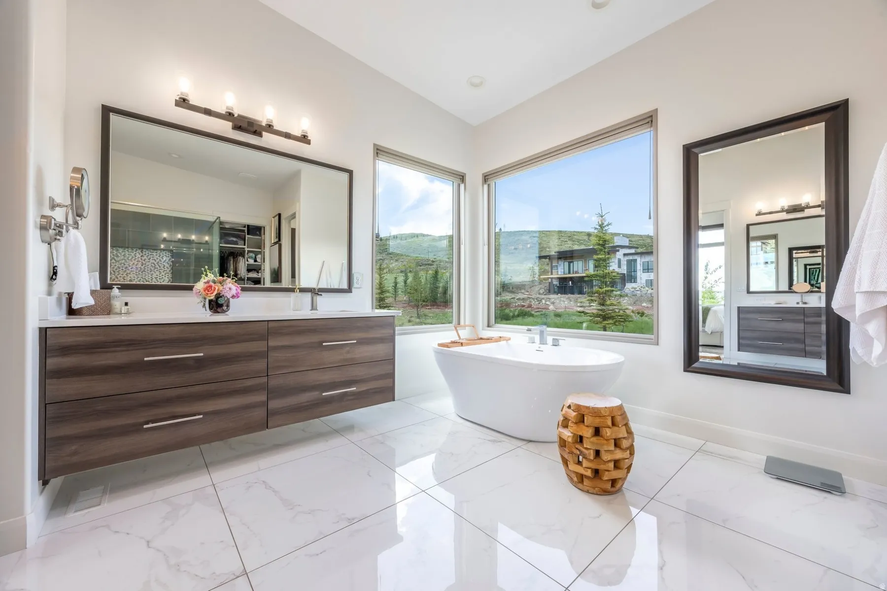 Freestanding soaking tub, dual floating vanity with white countertops, white tile flooring, and large windows