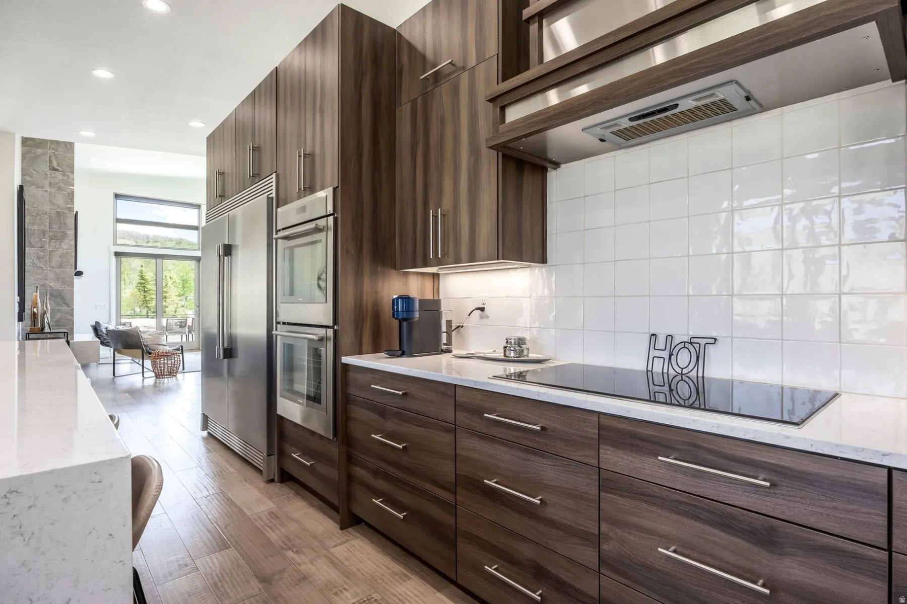 Integrated stainless steel appliances, wood-finish flooring, white subway tile backsplash, and light-toned countertops