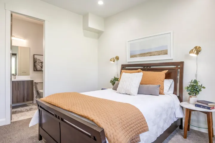 Recessed ceiling lighting, wall-mounted sconces, light gray carpeting, and an ensuite bathroom featuring a vanity with wood-finish cabinetry