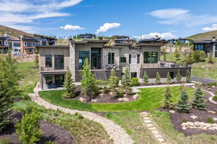 Modern contemporary exterior with stone and wood-panel accents, multiple outdoor terraces, and a meticulously landscaped yard