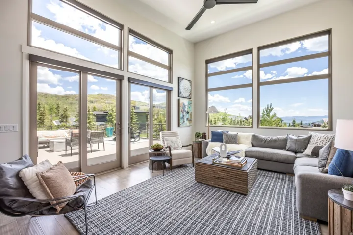 Expansive floor-to-ceiling windows, soaring ceiling height, wood-finish flooring, and a contemporary ceiling fan